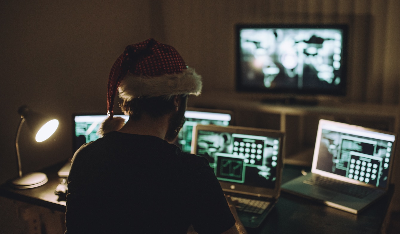 Hacker devant plusieurs écrans d'ordinateur avec un bonnet de Noël
