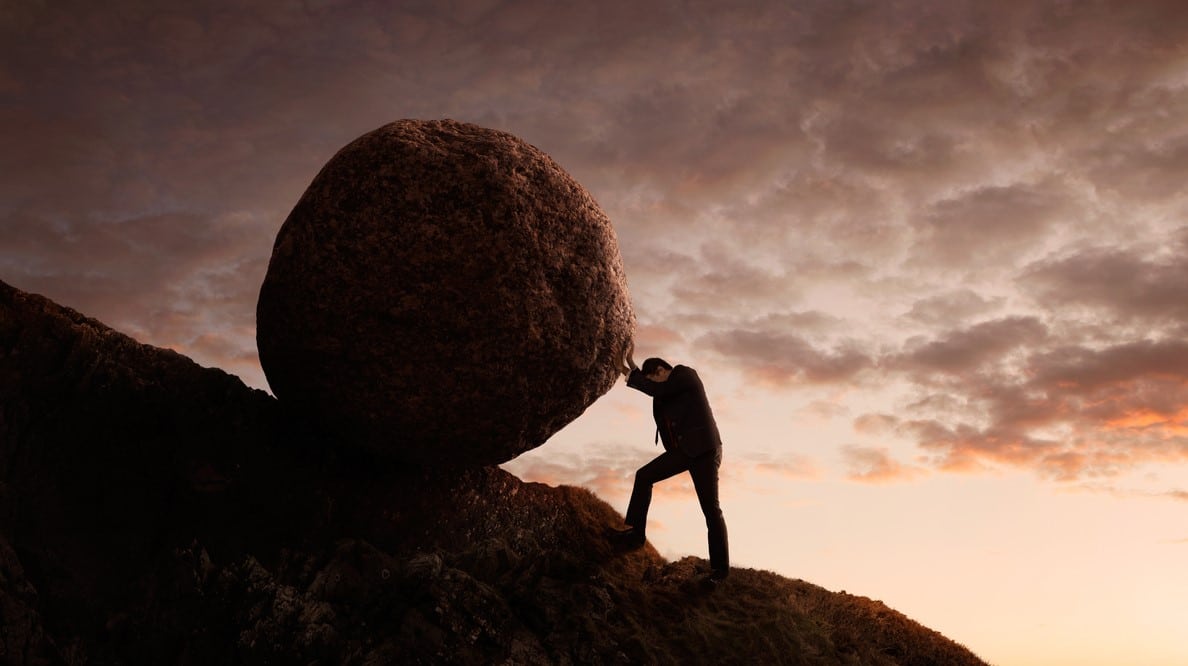 Un homme pousse un rocher en haut d'une montagne.