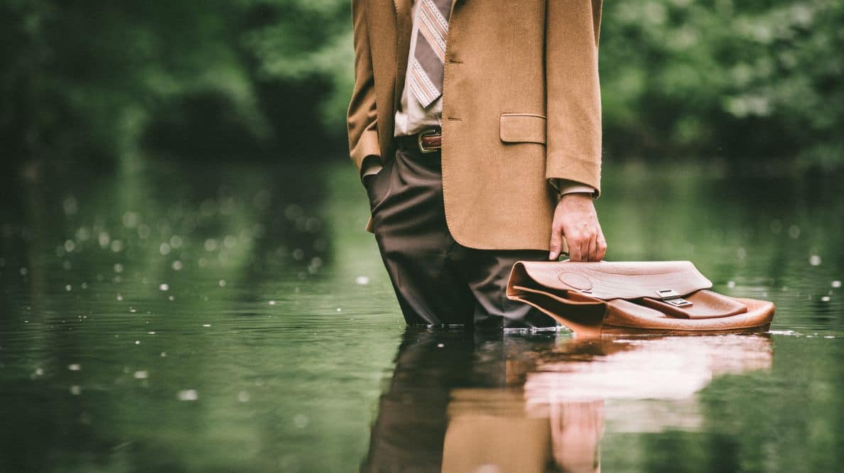 Un homme en costume-cravate les jambes dans l'eau à cause d'une inondation