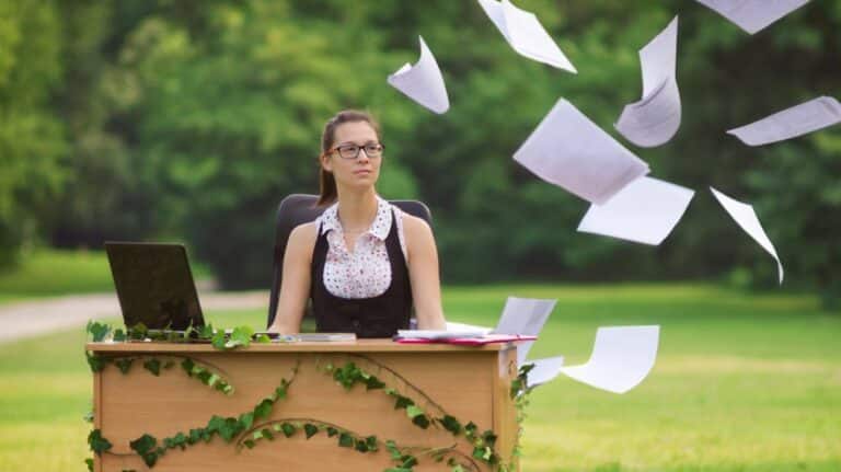 Une femme travaillant sur un bureau avec du lierre et des feuilles de papier volant autour d'elle