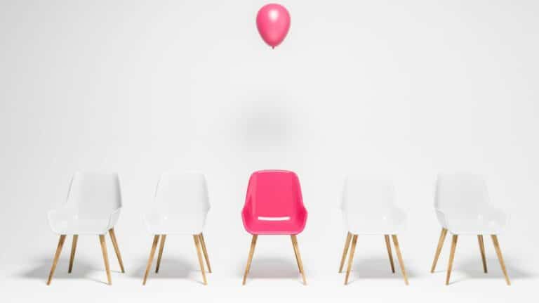 4 chaises blanches et une chaise rose au-dessus de laquelle flotte un ballon de baudruche rose