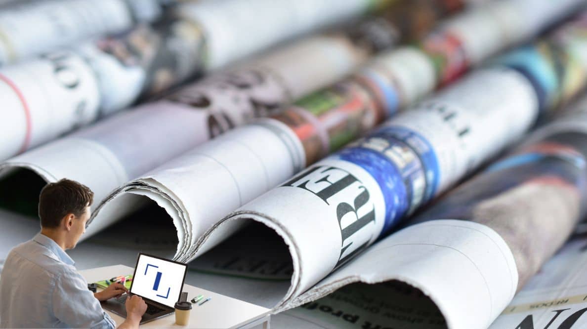 Un homme travaillant sur son ordinateur devant des journaux pliés