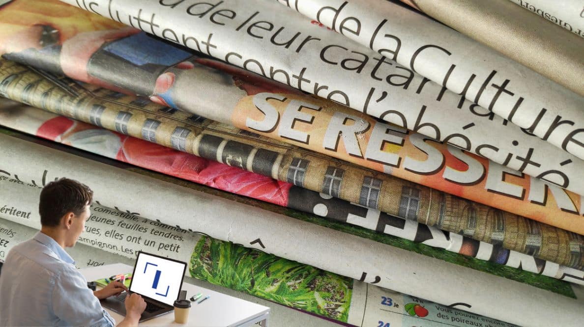 Un homme travaillant sur son ordinateur devant une pile de journaux